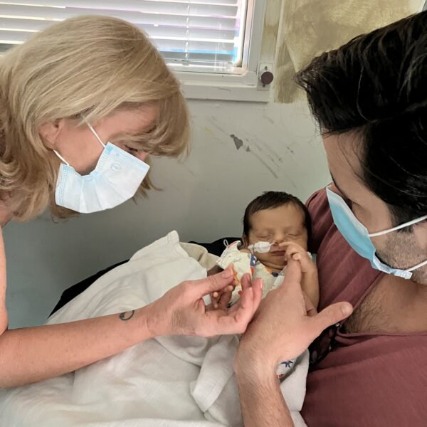 Gabriela being held in the hospital by her father and holding Grandma's hand.